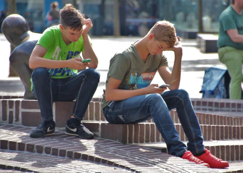 two young people sitting watching the phone in a park