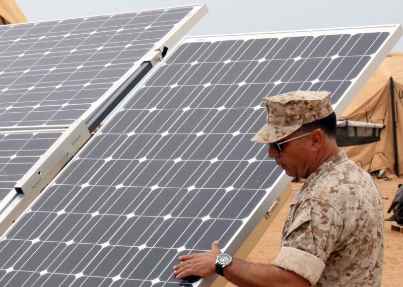 service members next to solar panels