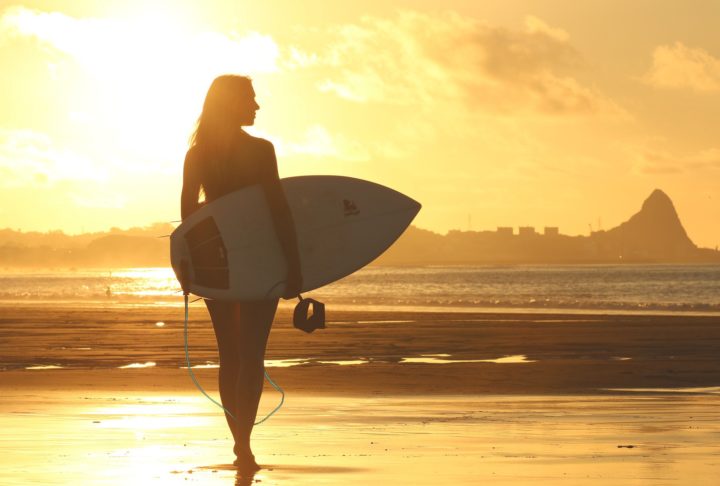 surfer girl walking in the shore at sunset