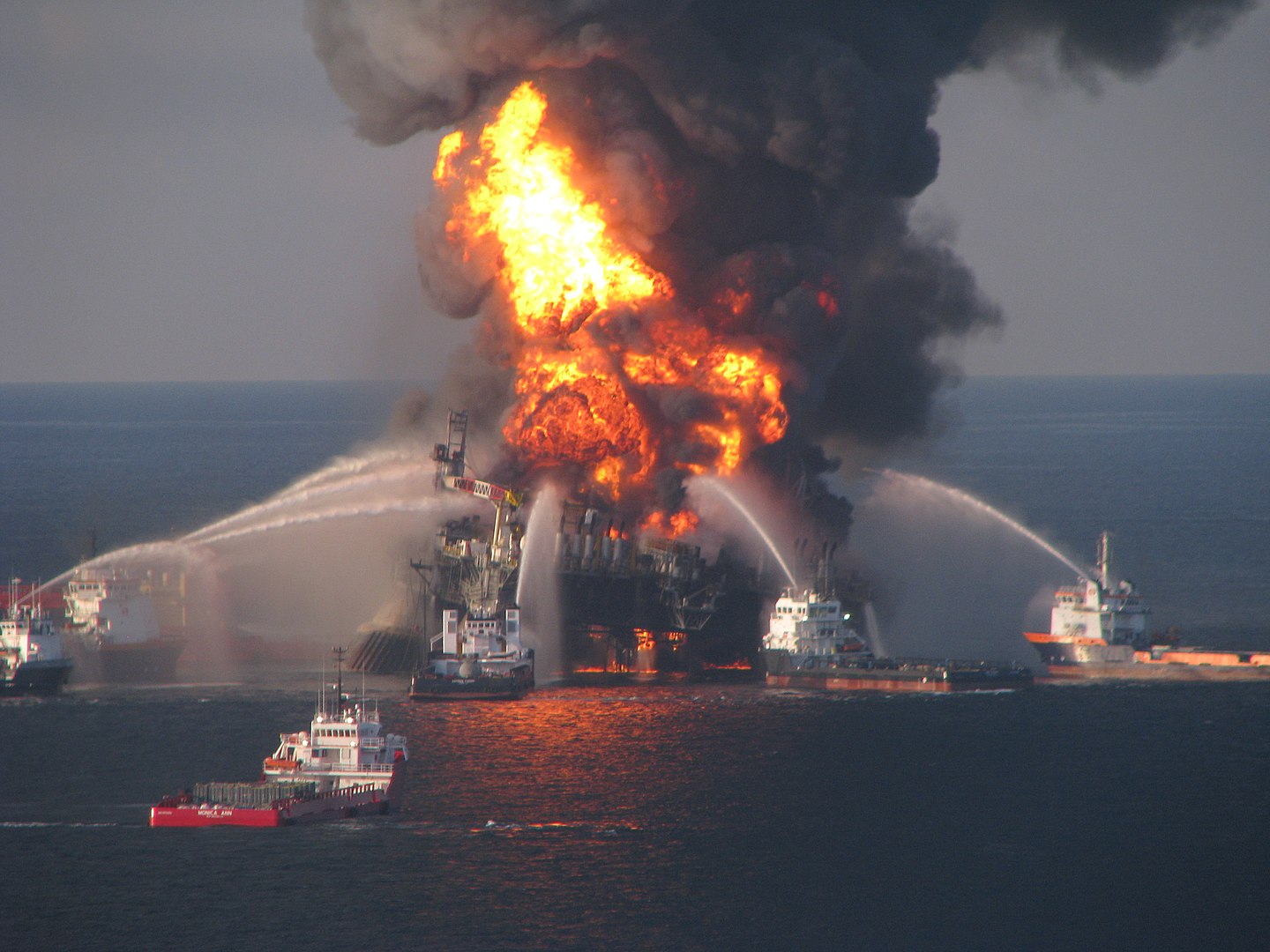 oil rig on fire with boats spraying water on it