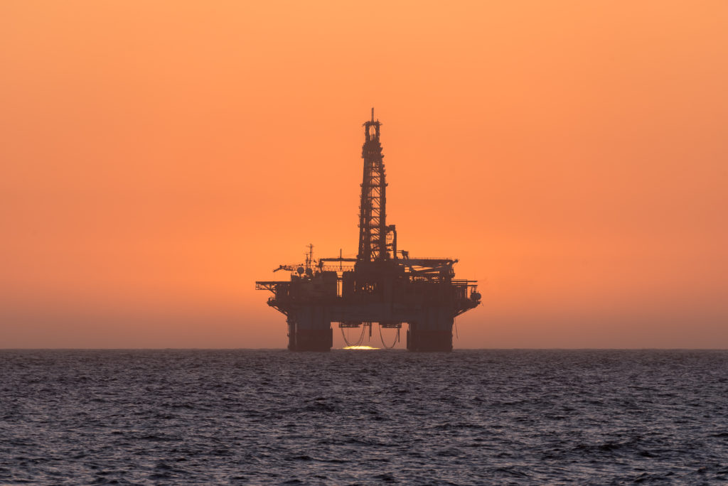 The sun is setting behind an oil drilling platform