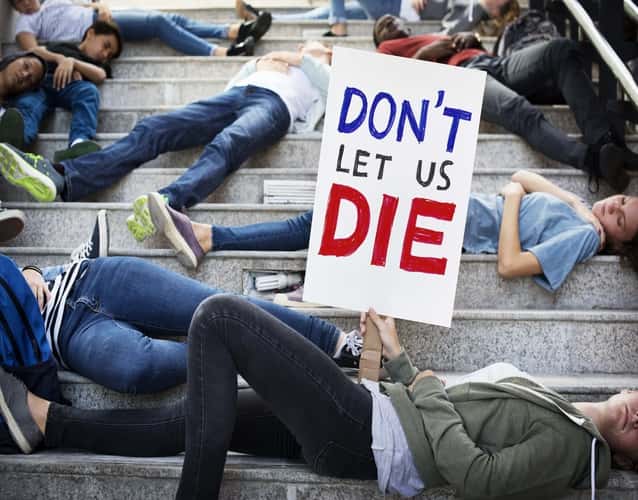 don't let us die sign held by a woman lying on steps during protest