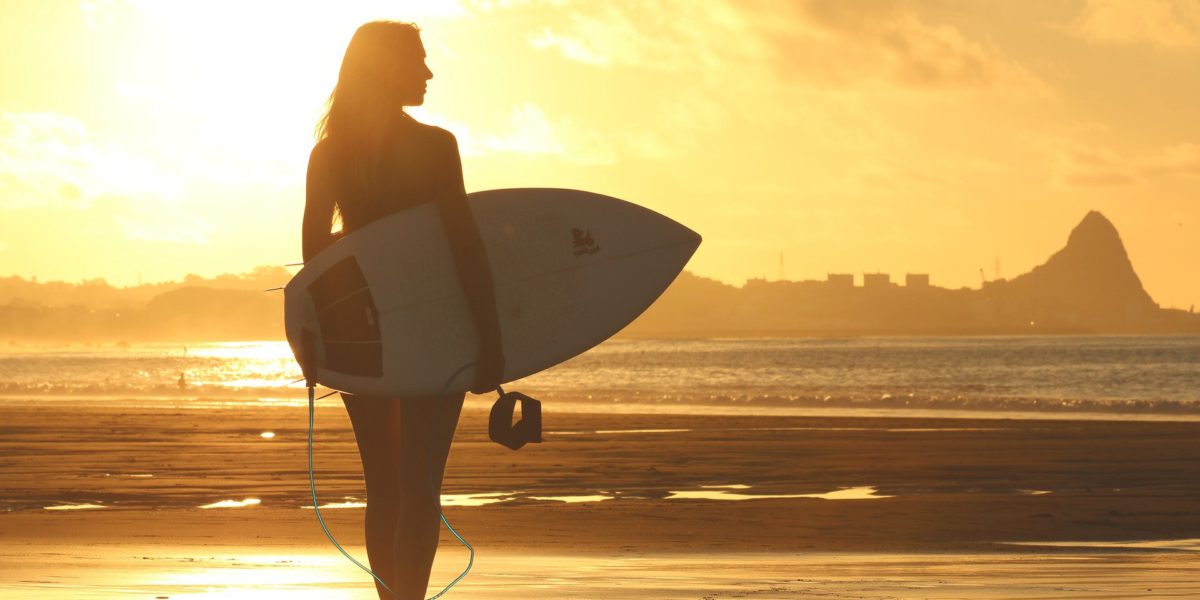 surfer girl walking in the shore at sunset