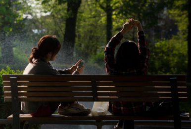 two girls sitting on a bench, one watching the phone and the other girl stretching