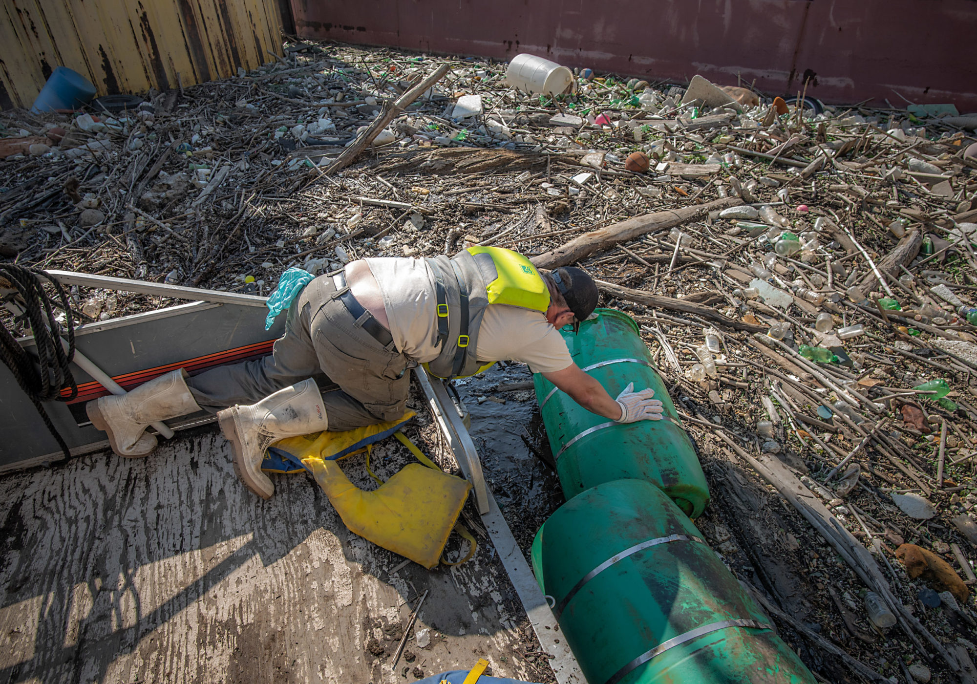Evan Clark, a boat captain with the non-profit Allegheny CleanWays, tries to pull a plastic barrel from a debris island floating in the Monongahela River. CREDIT: Teake Zuidema/Nexus Media News