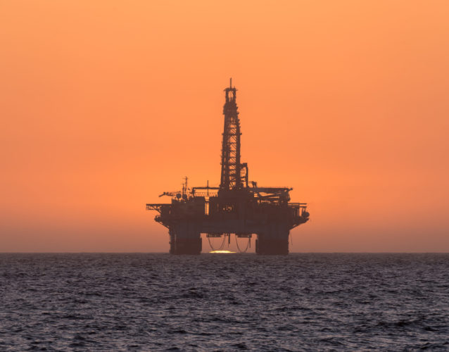 The sun is setting behind an oil drilling platform